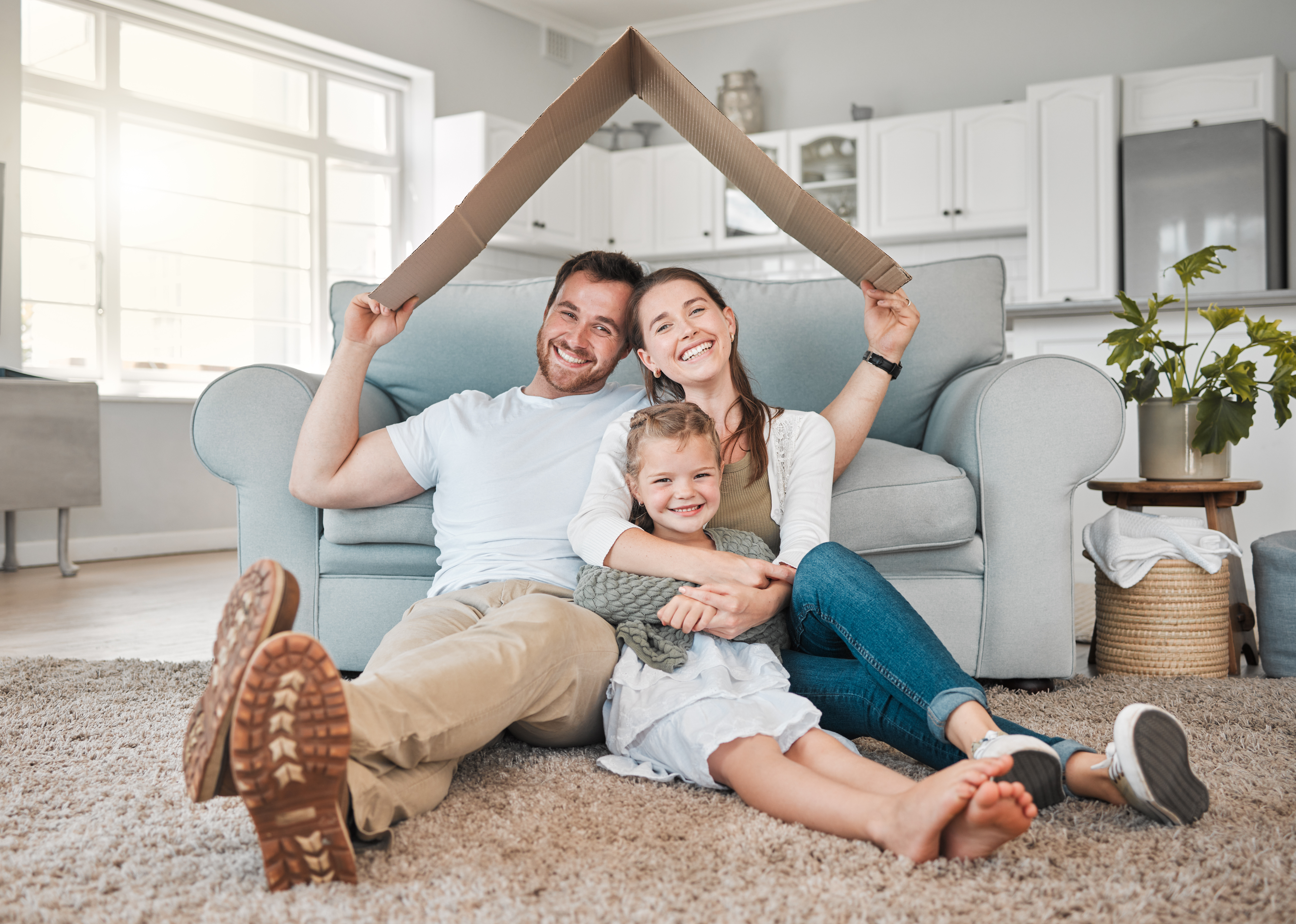 Family in apartment living room holding a carboard roof over their head.